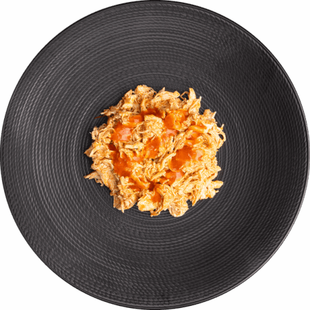 Spicy shredded buffalo chicken in black meal-prep tray.